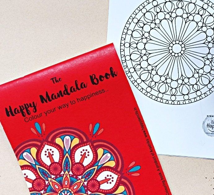 The Happy Mandala Book, a red-covered colouring book, next to an unfinished mandala page on cream paper